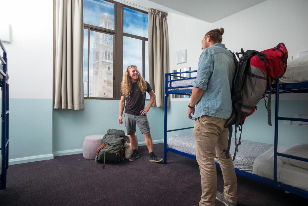 Yha Sydney Central Exterior photo The photo shows two young men in a room that appears to be a hostel or shared accommodation. One man has long hair and is standing next to a backpack on the floor, appearing relaxed or amused. The other man, with shorter hair tied back, is standing w