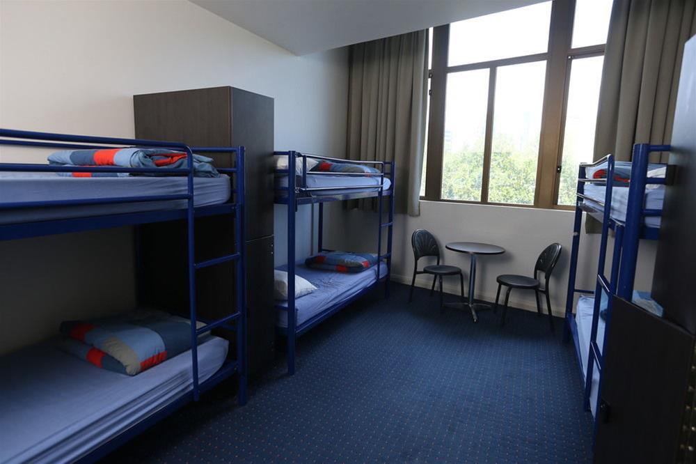 Yha Sydney Central Exterior photo The photo shows a dormitory-style room featuring two sets of bunk beds, accommodating a total of four sleeping areas. The beds have blue metal frames and are covered with plain bedding. In the center of the room, there is a small round table with two