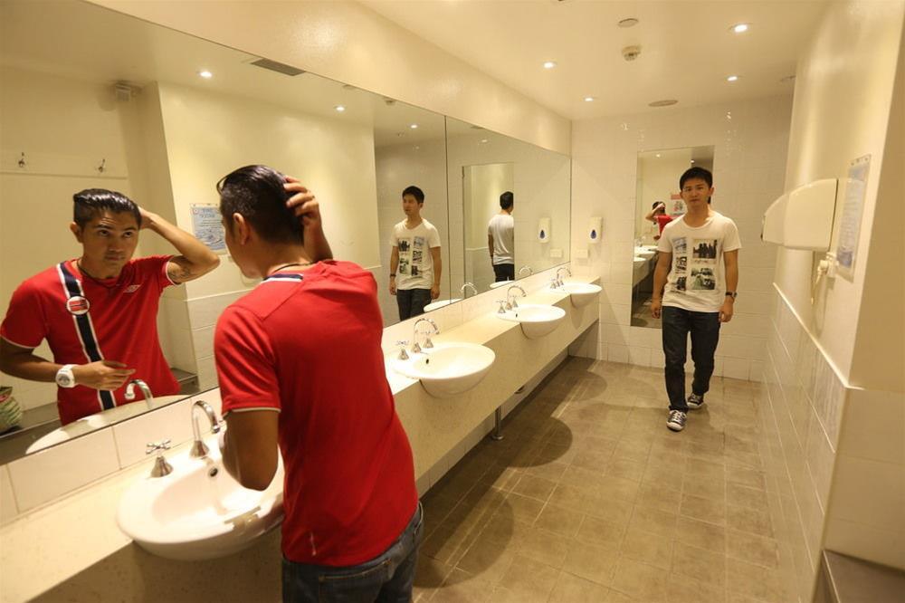 Yha Sydney Central Exterior photo The photo shows a modern public bathroom. There are several sinks along one wall, with mirrors above them. In the foreground, a person in a red shirt is fixing their hair while standing in front of one of the sinks. In the background, another person 