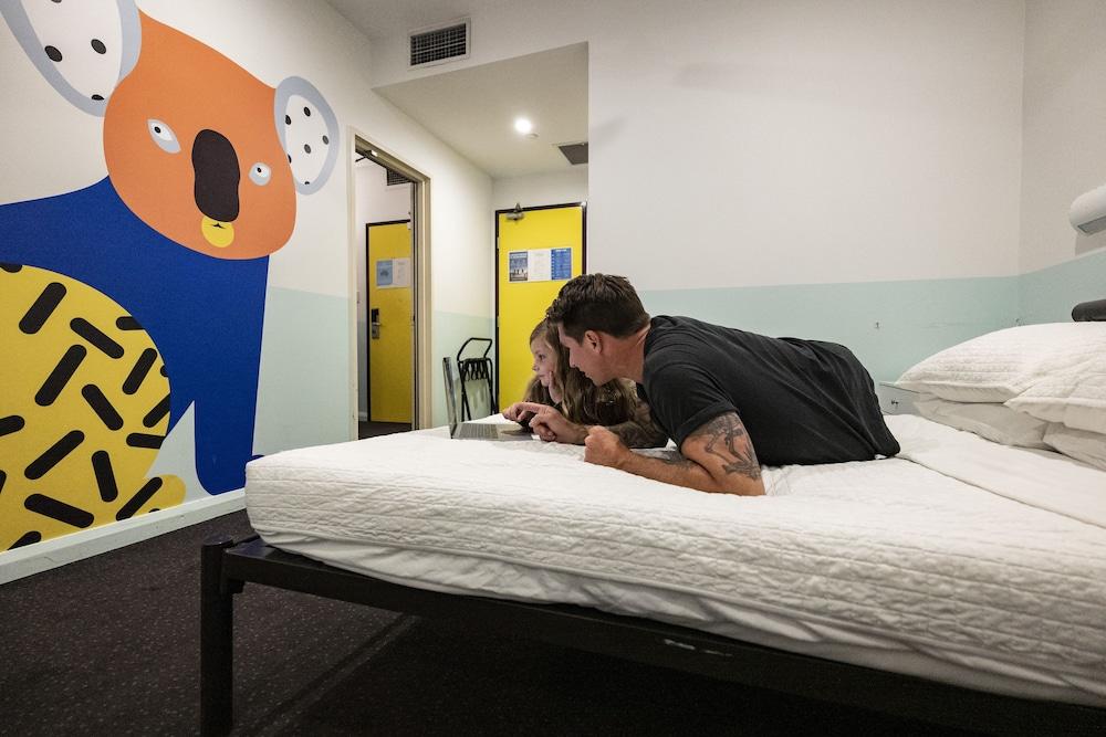 Yha Sydney Central Exterior photo The photo shows a couple lying on a bed in a room. They appear to be engaged in reading or looking at something together. The room features a colorful mural of a koala on one wall, adding a playful element to the space. There are doors visible in the