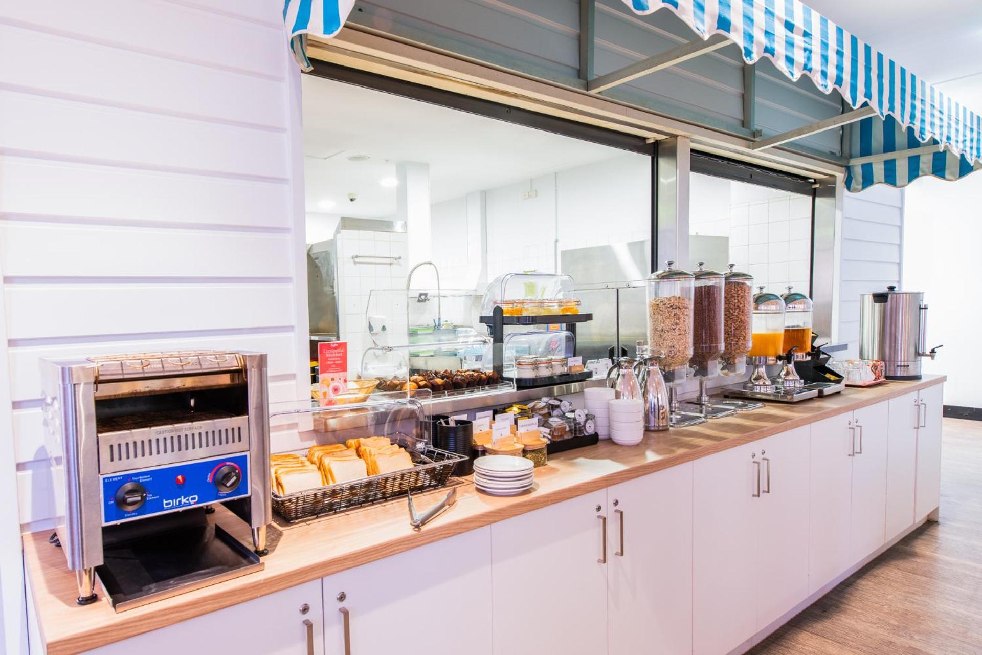 Yha Sydney Central Exterior photo The photo shows a breakfast buffet setup. On a counter with a light-colored wooden surface, there are various food and drink items. 

To the left, there is a toaster, and next to it, a basket with pastries or bread. There are also several containers 