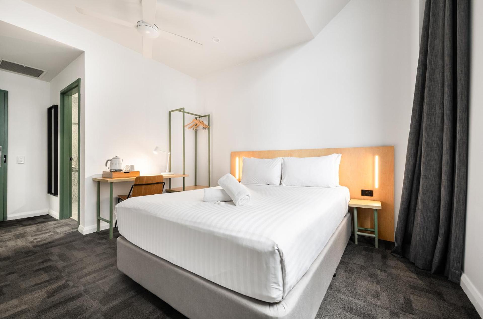 Yha Sydney Central Exterior photo The photo shows a modern hotel or guest room. It has a neatly made bed with white blankets and pillows. Next to the bed, there are two bedside lamps. A small desk and chair are visible, along with a kettle on the desk. There’s a clothing rack in the 