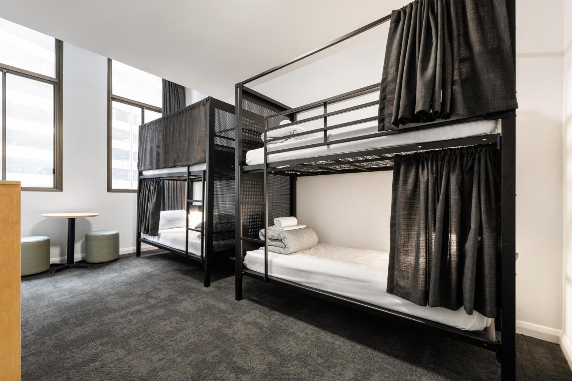 Yha Sydney Central Exterior photo The photo shows a modern dormitory room featuring two sets of black metal bunk beds. Each bunk has white bedding and neatly arranged towels. The beds are partially enclosed with black curtains for privacy. There are large windows letting in natural l