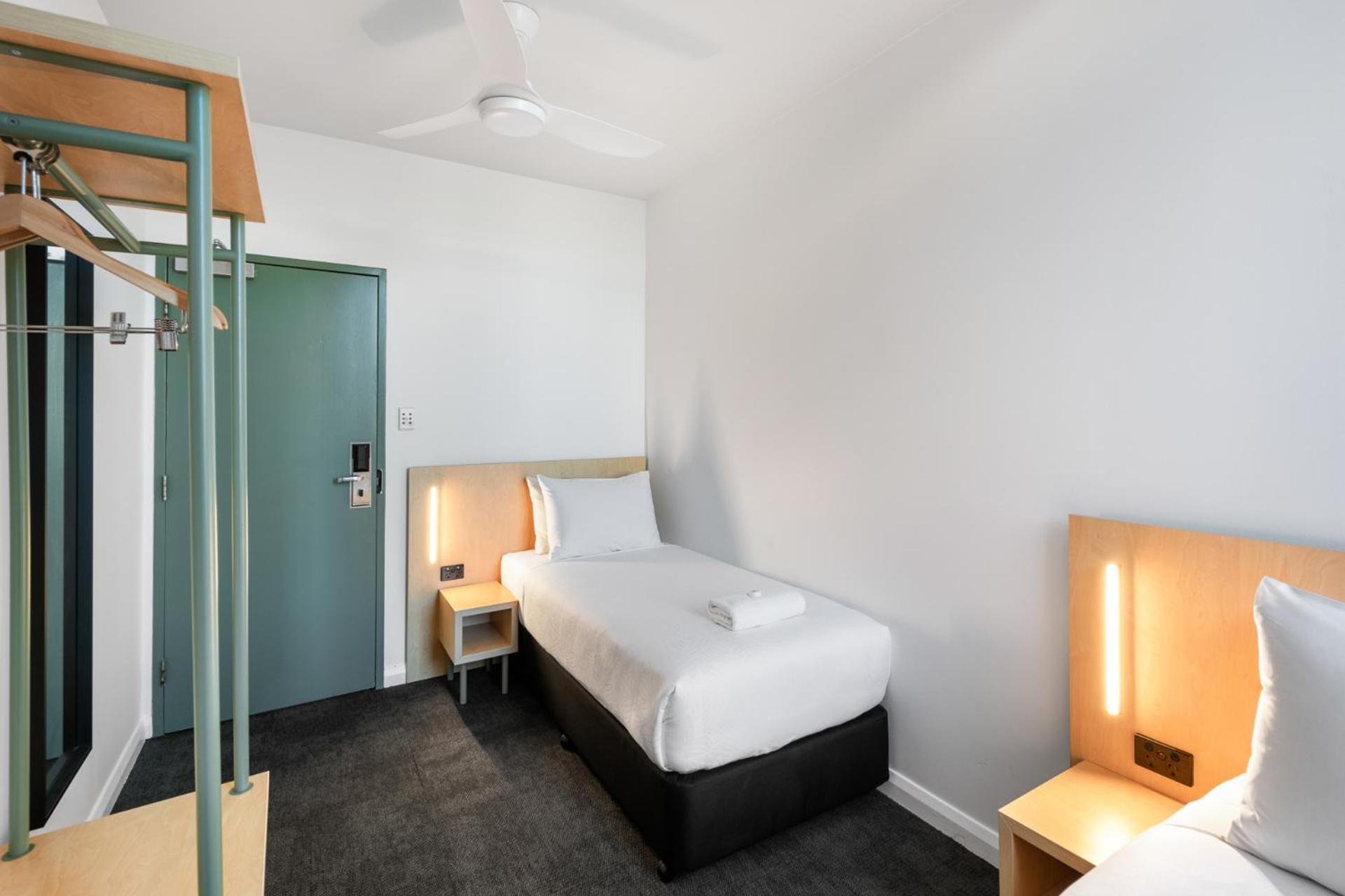 Yha Sydney Central Exterior photo The photo shows a simple and modern hotel room. It features two single beds with white linens and a small bedside table on each side, equipped with light fixtures. One wall includes a green door, likely leading to the hallway, and there is a clothing