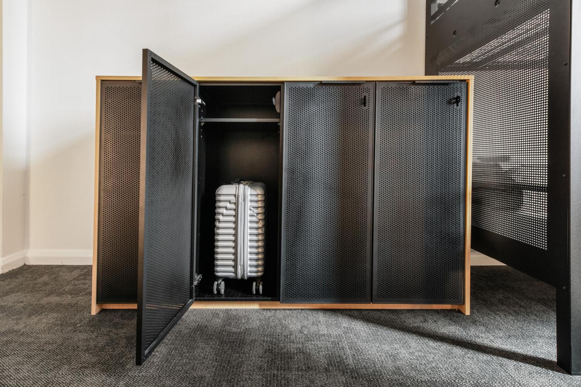 Yha Sydney Central Exterior photo The photo shows a modern piece of furniture, likely a cabinet or storage unit, with its doors open. Inside, there is a suitcase, which is white with a textured design, resting on its wheels. The cabinet has a minimalist design, featuring a wood frame