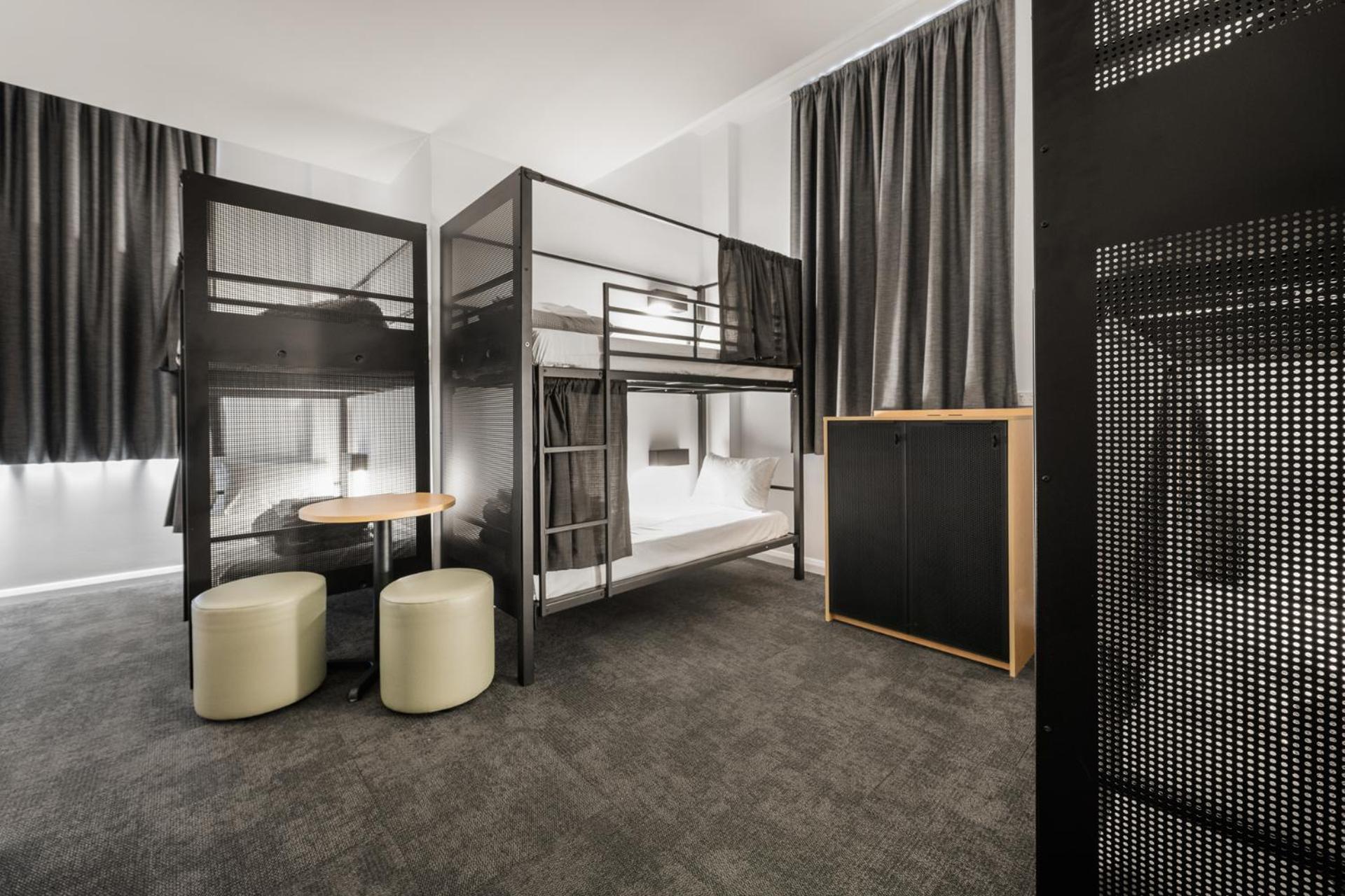 Yha Sydney Central Exterior photo The photo depicts a modern bedroom or dormitory setting. It features a lofted bunk bed with a metal frame, providing sleeping space above and possibly storage or a seating area below. There are two round stools made of a light-colored material positi
