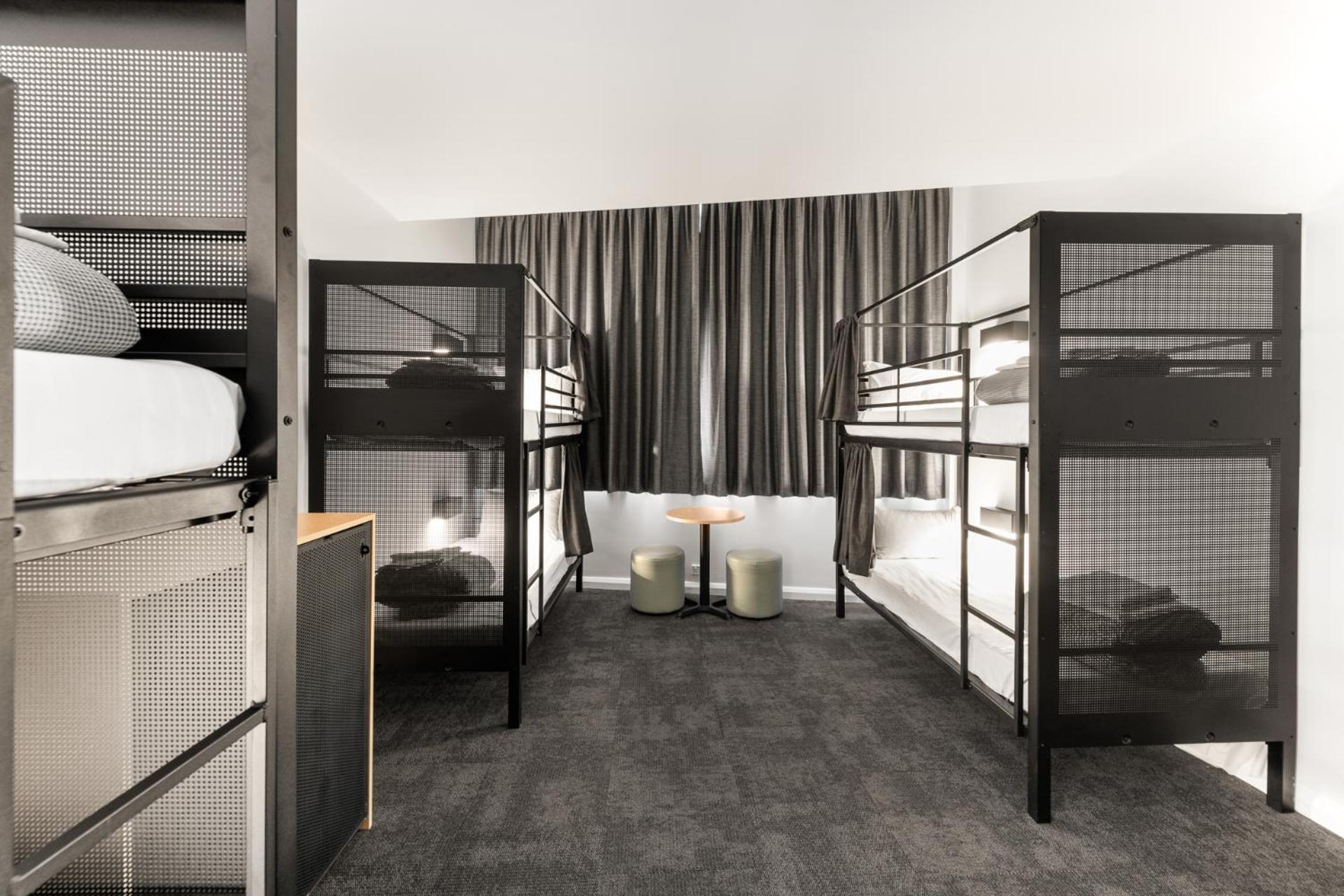 Yha Sydney Central Exterior photo The photo shows a modern bunk bed room designed for accommodation, likely in a hostel or shared living space. There are two sets of black metal bunk beds, each with neatly made beds. The room features a neutral-colored carpet and large, floor-to-ceil