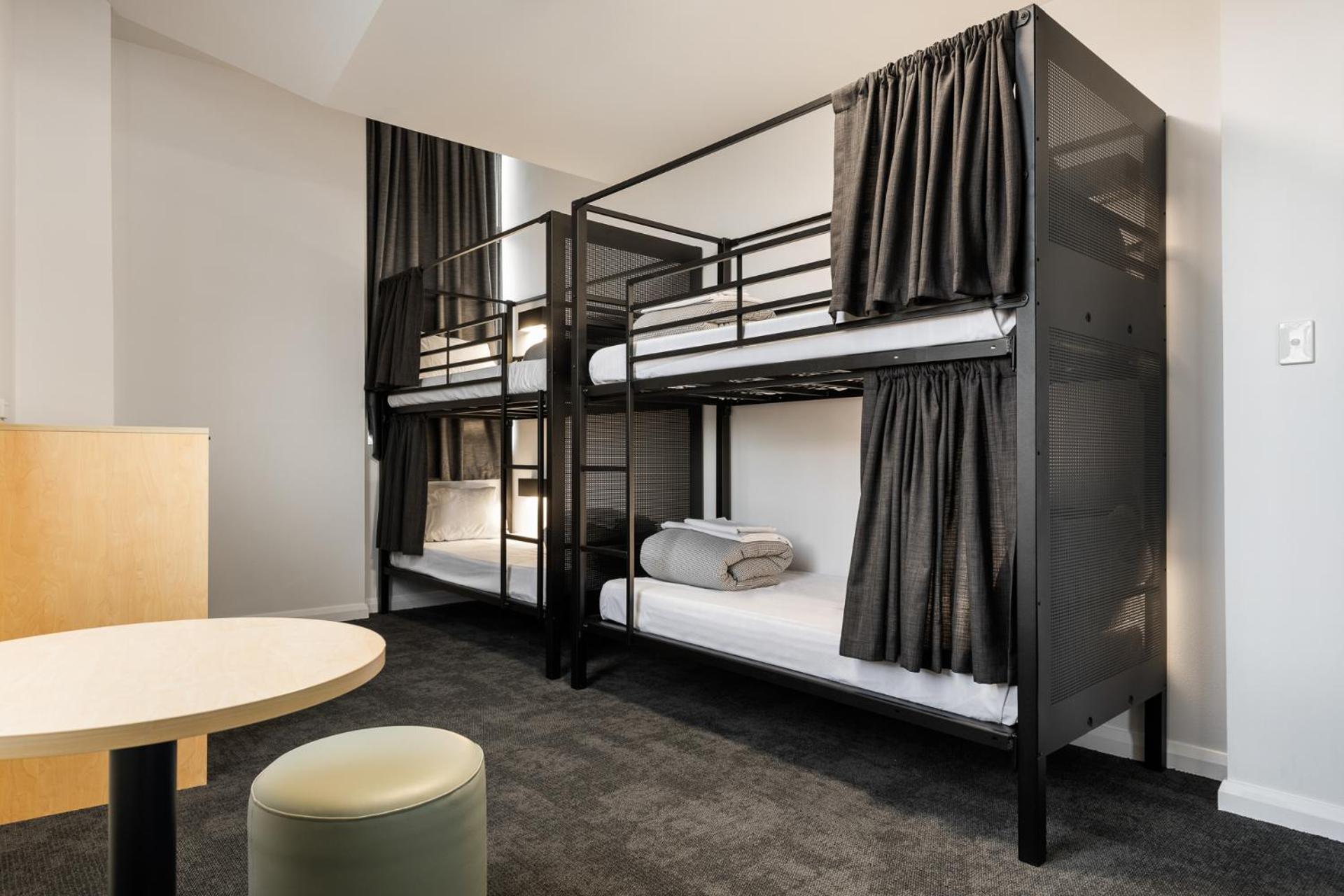 Yha Sydney Central Exterior photo The photo shows a modern sleeping area featuring two bunk beds. Each bunk bed has black metal frames and is equipped with bedding, including mattresses, pillows, and neatly folded blankets. The beds are enclosed with dark curtains, providing privacy.