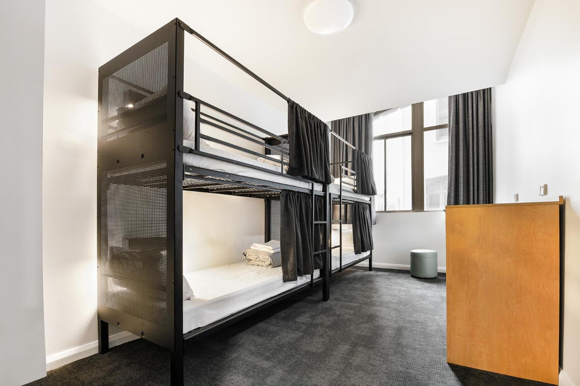 Yha Sydney Central Exterior photo The photo shows a modern shared dormitory room featuring two sets of bunk beds. The beds are made with clean white linens, and each bunk has a privacy curtain. The room is well-lit with natural light coming from large windows, which are covered with 