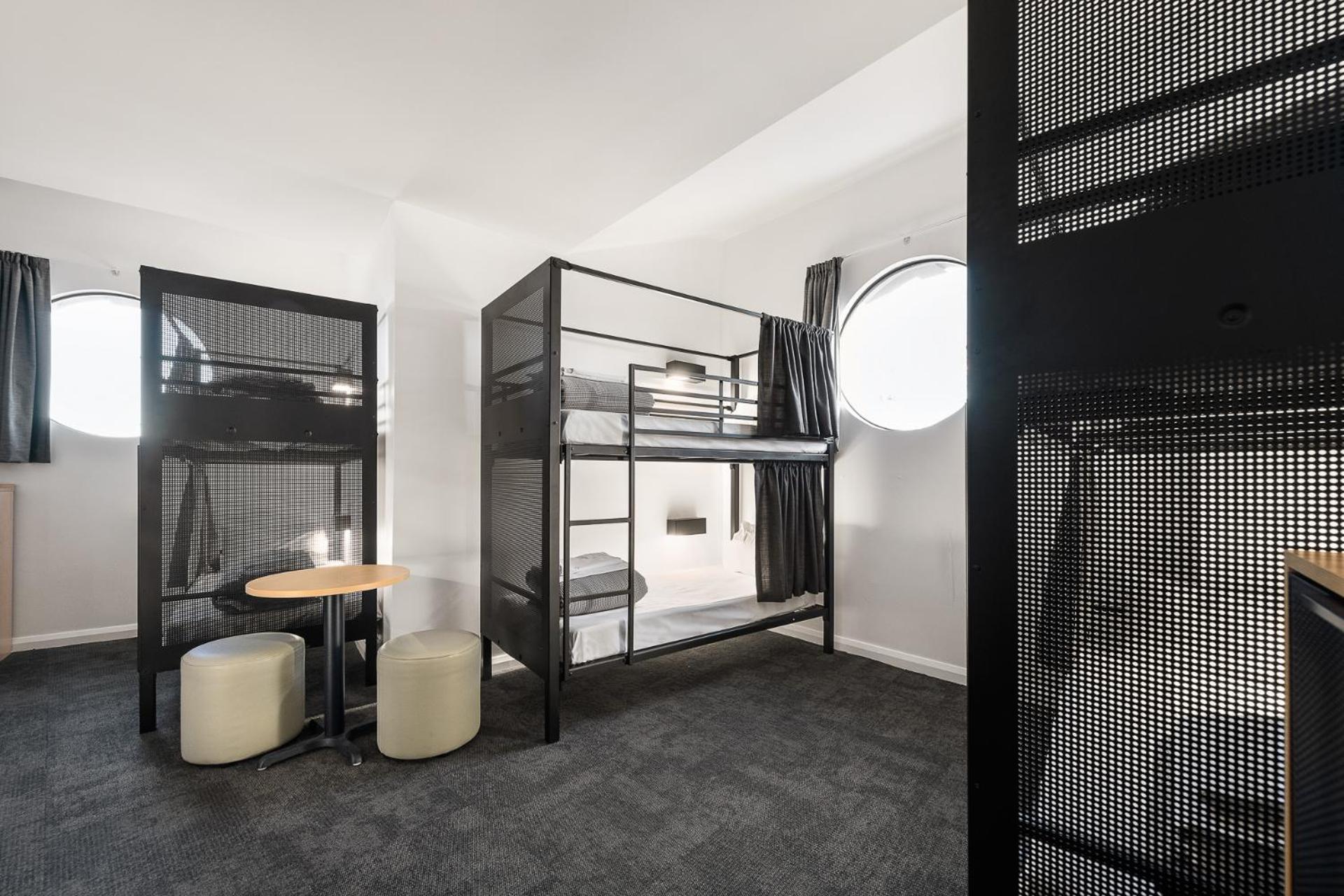 Yha Sydney Central Exterior photo The photo shows a modern dormitory-style room with two metal bunk beds. Each bunk has a simple design with a mesh-like structure, and the top bunk is accessible via a ladder. The room is brightly lit and features circular windows that allow natural l